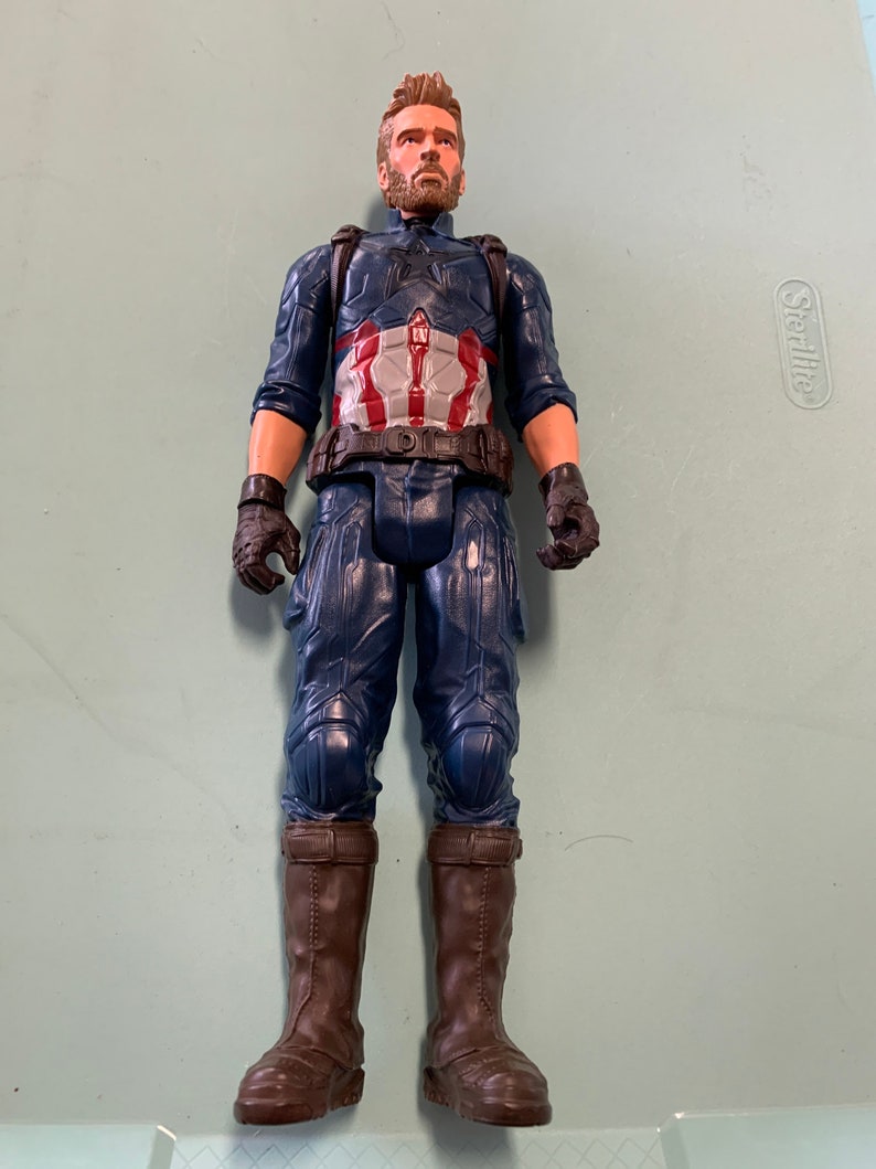 May include: A plastic action figure of Captain America wearing a blue and red costume with a brown belt and brown boots. The figure has a beard and short brown hair.