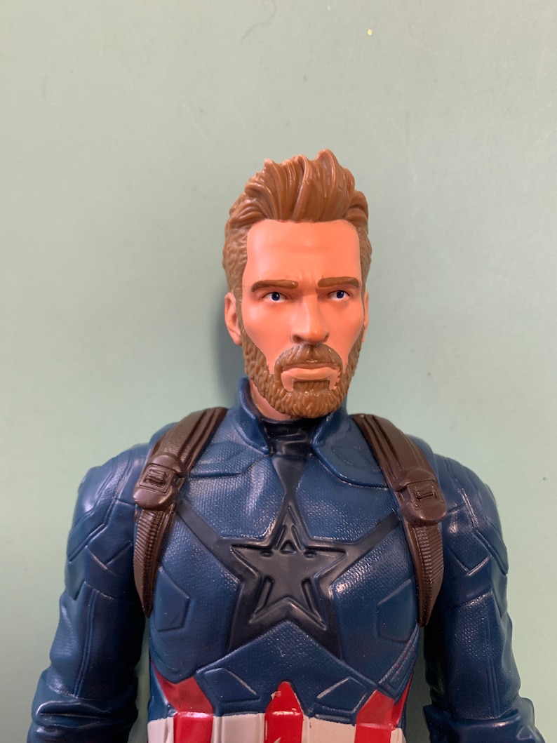 May include: A plastic action figure of Captain America wearing a blue and red costume with a star on the chest. He has a brown beard and brown hair.