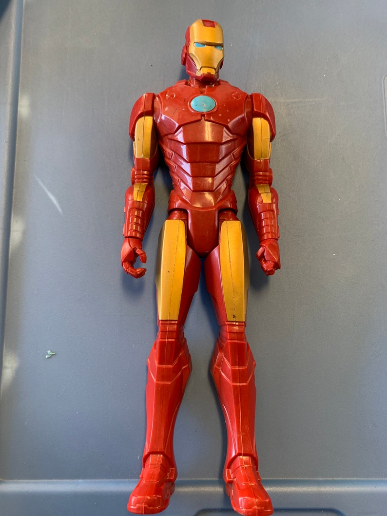 K&ouml;nnte beinhalten: Eine rote und goldene Iron Man Actionfigur mit einer blauen Gesichtsmaske. Die Figur steht auf einer blauen Oberfl&auml;che.