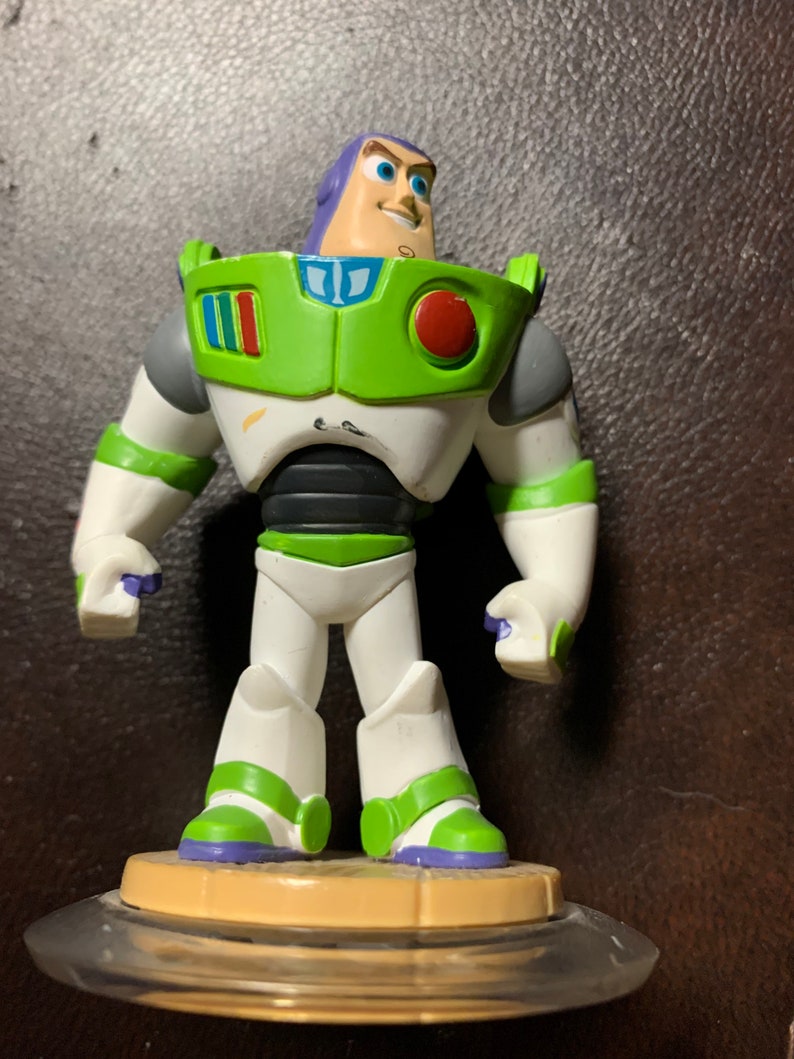 May include: A green and white plastic action figure of Buzz Lightyear from the Toy Story franchise. The figure is standing on a clear plastic base with a brown center.