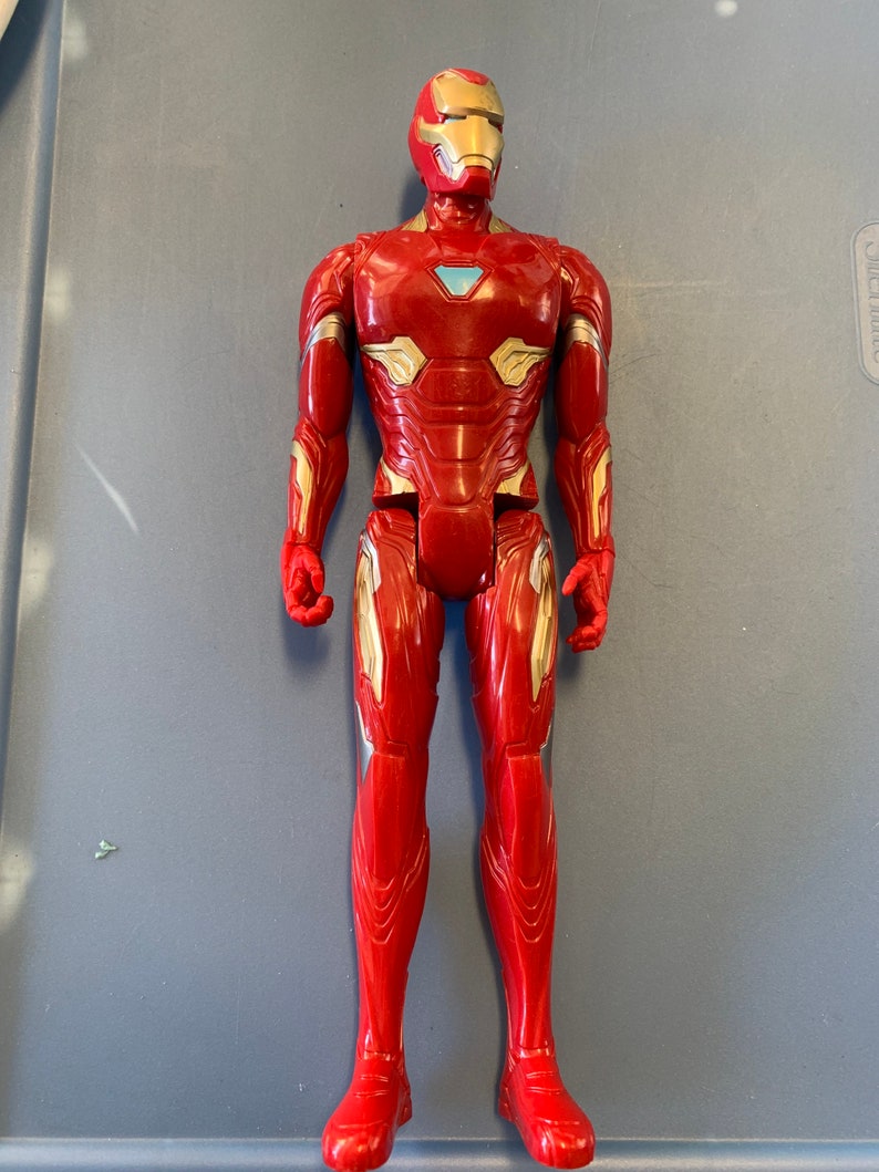 May include: A red and gold action figure of Iron Man, a superhero from the Marvel universe. The figure is posed standing with its arms at its sides. The figure has a detailed design with a red and gold suit and a blue and silver face mask.