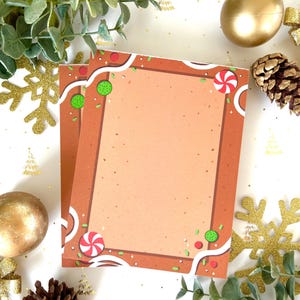 Könnte beinhalten: Zwei leere Karten im Lebkuchen-Design mit braunem Hintergrund und weißen Zuckerguss-Akzenten. Die Karten sind mit roten und grünen Süßigkeiten, Streuseln und weißem Zuckerguss verziert. Die Karten sind von goldenen Ornamenten, Tannenzapfen und Grün umgeben.