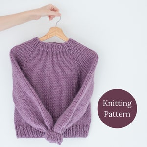 May include: A lilac knitted sweater hangs on a wooden hanger. The sweater has a crew neck and long sleeves. The image includes a circular graphic with the words "Knitting Pattern".