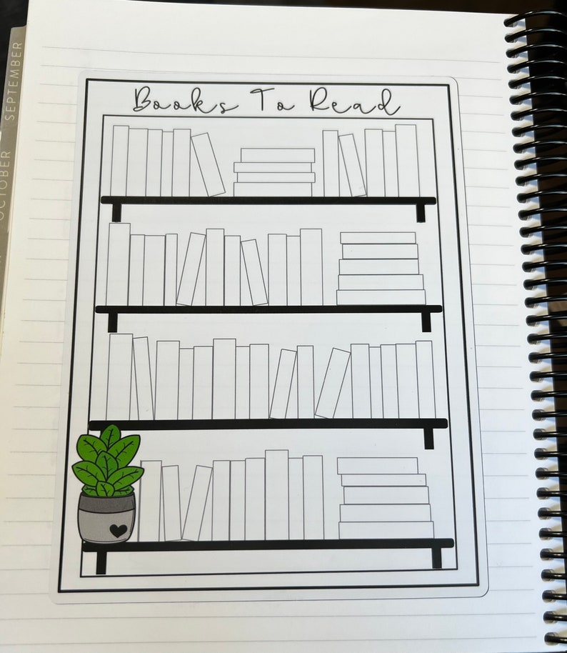 May include: A rectangular sticker featuring a black and white line drawing of a bookshelf with four shelves filled with blank book spines. The text Books To Read is printed at the top. A small potted green plant with a heart icon sits on the bottom shelf.