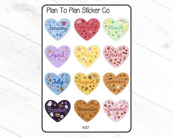 May include: A sheet of stickers from Plan To Plan Sticker Co. featuring twelve heart-shaped designs, each representing a month of the year. Each heart is a different color and decorated with seasonal illustrations and the month's name.