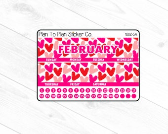 以下が含まれることがあります： ピンクと赤のハート模様の2月のステッカーシート。「FEBRUARY」の文字が大きなピンク色の文字で書かれています。週の曜日は上部に、日付は下部に記載されています。ステッカーシートには「Plan To Plan Sticker Co.」と記載されています。