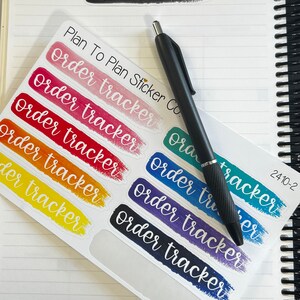 K&ouml;nnte beinhalten: Ein Blatt mit bunten Aufklebern f&uuml;r die Auftragsverfolgung mit einem schwarzen Stift darauf. Die Aufkleber sind in einem Regenbogen von Farben gehalten und haben den Text "order tracker" in Wei&szlig; auf jedem Aufkleber. Der Text "Plan To Plan Sticker Co." ist oben auf dem Blatt sichtbar.