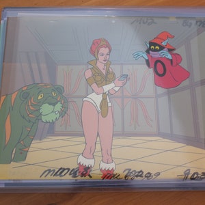 May include: A cel animation from the She-Ra: Princess of Power cartoon. She-Ra is standing in a room with a tiger and a red-robed figure. She-Ra is holding a small bottle in her hand. The animation is signed by the artist, "Maura McGreggor 7-03-89".