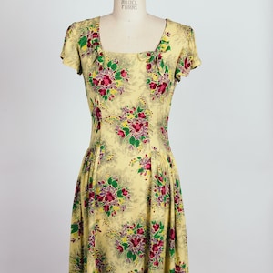 May include: A yellow maxi dress with a floral print featuring red, pink, and green flowers. The dress has a square neckline and short sleeves.
