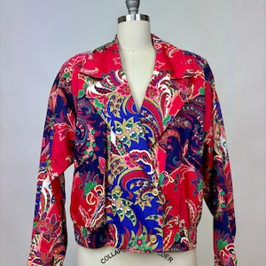 May include: A red, blue, and white paisley patterned jacket with a double breasted closure and gold buttons.