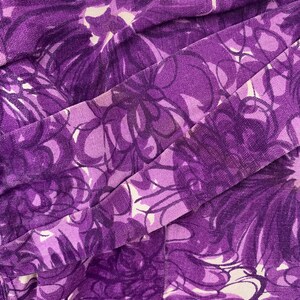 以下が含まれることがあります： 白と紫の抽象的な花柄の紫色の生地。生地は折り畳まれており、表面にテクスチャがあります。