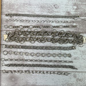 Op de afbeelding: Een verzameling van negen zilveren kettingen in verschillende lengtes en stijlen, gelegd op een houten oppervlak.
