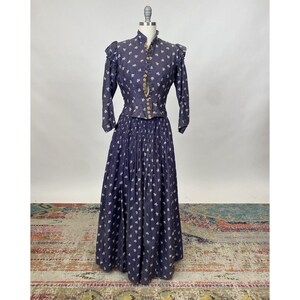 May include: A vintage two-piece dress with a fitted bodice and a full skirt. The dress is made of a dark blue fabric with a white floral pattern. The bodice has a high neckline and a button-up front. The skirt is pleated and falls to the floor.