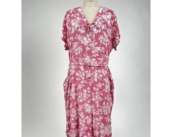Könnte beinhalten: Ein rosa Kleid mit floralem Muster, weißem Kragen, kurzen Ärmeln und einer Knopfleiste vorne. Das Kleid hat einen Knoten am Hals und einen Gürtel in der Taille.