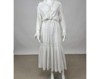 May include: A white maxi dress with long sleeves and a ruffled neckline. The dress has a gathered waist and a tiered skirt with lace trim.