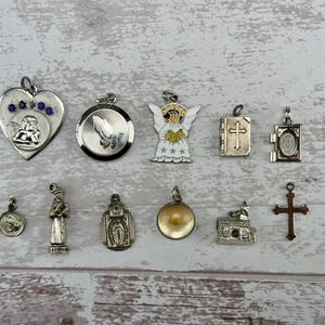 Peut inclure: Une collection de 12 pendentifs de charme en argent et en or sur le thème religieux, comprenant un cœur avec des pierres bleues, un ange, une croix, une église et un livre.