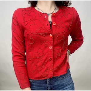 May include: A red cardigan sweater with a heart pattern. The cardigan has a button closure and long sleeves.