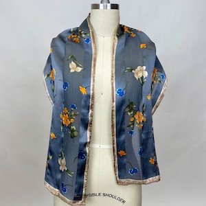 May include: A grey silk scarf with a floral pattern in shades of blue, orange, and white. The scarf has a brown trim.
