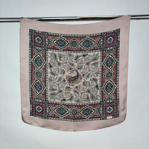 May include: A pink silk scarf with a paisley pattern and a border of geometric designs in shades of red, blue, and gold.