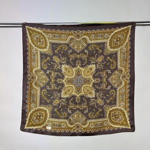 May include: A brown silk scarf with a paisley pattern in shades of gold and brown. The scarf has a square shape and a fringed edge.