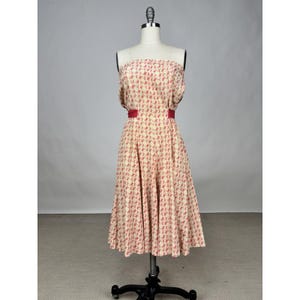 May include: A strapless dress with a cream background and a red floral pattern. The dress has a red ribbon around the waist and a full skirt.
