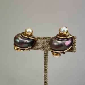 Könnte beinhalten: Ein Paar goldfarbene Ohrringe mit einem schwarzen und irisierenden Muscheldesign und einem weißen Perlenakzent.