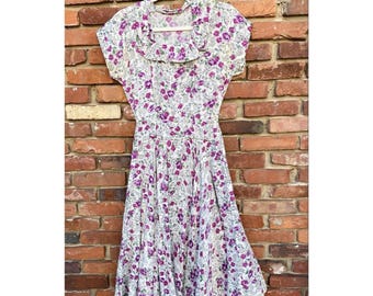 Könnte beinhalten: Ein weißes Kleid mit lila Blumenmuster und einem Rüschenkragen. Das Kleid hat kurze Ärmel und einen vollen Rock.