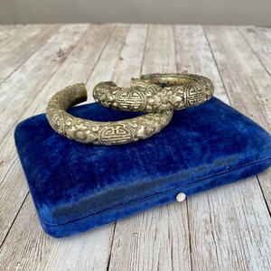 Puede incluir: Dos pulseras de plata con intrincados diseños florales y geométricos, descansando sobre una caja de terciopelo azul.
