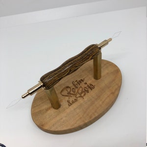 Peut inclure: Un outil en bois avec une poignée en laiton et une pointe en forme d'aiguille, reposant sur une base en bois avec l'inscription "Robin des Bois".