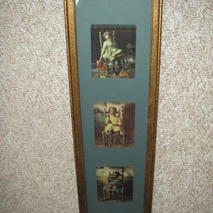 May include: A framed artwork featuring three vintage prints of a child in a chair. The frame is gold-colored with a textured design. The prints depict a child in different colored dresses.