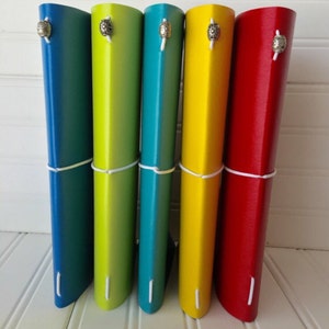 May include: Five leather-bound journals with a gradient color design. The journals are teal, yellow, blue, yellow, and red. Each journal has a silver button closure.