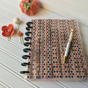 May include: A brown and white polka dot journal with a black spiral binding. The journal has a wood grain pattern and a gold pen with a clear crystal tip.