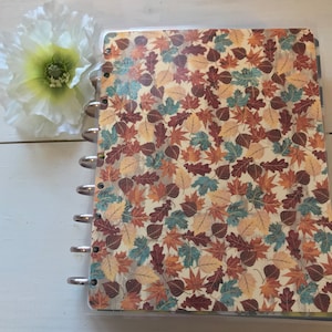 May include: A clear plastic binder with a fall-themed leaf pattern in shades of brown, orange, red, and blue. The binder has a silver ring mechanism.