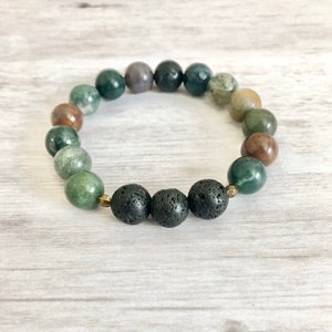 May include: A green and brown agate gemstone bracelet with black lava rock beads. The bracelet is made with natural stones and is designed to be worn on the wrist.