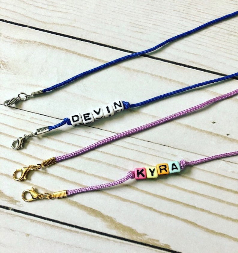 Op de afbeelding: Drie kleurrijke kralenkettingen met metalen sluitingen. De kettingen spellen de namen "Devin" en "Kyra" uit.