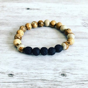 May include: A brown and beige gemstone bracelet with black lava rock beads. The bracelet is made of natural stones and is designed to be worn on the wrist.