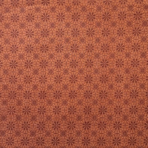 May include: A repeating pattern of dark red circles with a wheel-like design on a light brown background. The circles vary in size and are evenly spaced, creating a symmetrical and detailed design. The overall effect is a textured, decorative pattern.