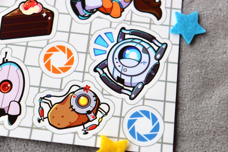 Puede incluir: Un conjunto de pegatinas con personajes del videojuego Portal. Las pegatinas est&aacute;n sobre un fondo blanco cuadriculado. Las pegatinas incluyen un pastel, una pistola portal, una patata y un robot.
