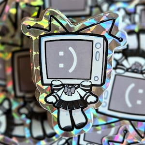 May include: A holographic sticker depicting a cartoon television character with a smiling face. The character is dressed in a sailor uniform with a black skirt and white top. The sticker has a silver, iridescent border.