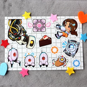 Puede incluir: Un conjunto de 11 pegatinas con personajes y objetos del videojuego Portal. Las pegatinas est&aacute;n impresas en papel blanco con un patr&oacute;n de cuadr&iacute;cula. Las pegatinas incluyen una pistola portal, un cubo compa&ntilde;ero, un pastel, una torreta y una patata.