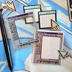 May include: A selection of stickers and a stylus pen. The stickers depict a retro computer interface, including a paint program window and cursor icons. The text "untitled-Paint" is visible. The background is a light blue fabric.