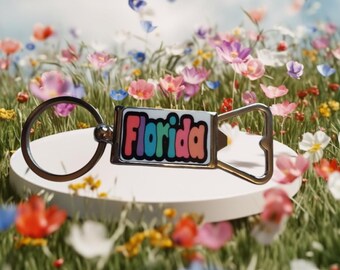 May include: A silver keychain with a bottle opener and a colorful rectangular tag that says "Florida". The keychain is sitting on a white surface surrounded by a field of colorful flowers.