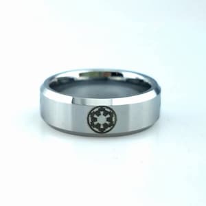 May include: A silver tungsten carbide ring with a beveled edge and a black and white engraved symbol.