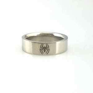 Peut inclure: Une bague en argent avec un logo Spiderman gravé sur la bande.