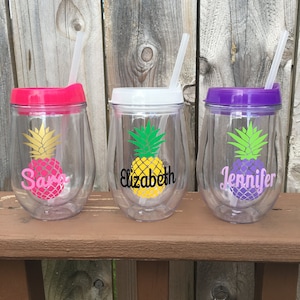 May include: Three clear plastic wine tumblers with lids and straws. Each tumbler has a pineapple design and a name on the front: Sara, Elizabeth, and Jennifer.