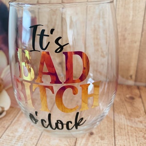May include: Clear glass wine glass with the text "It's Bad Bitch o'clock" in black and gold foil lettering.