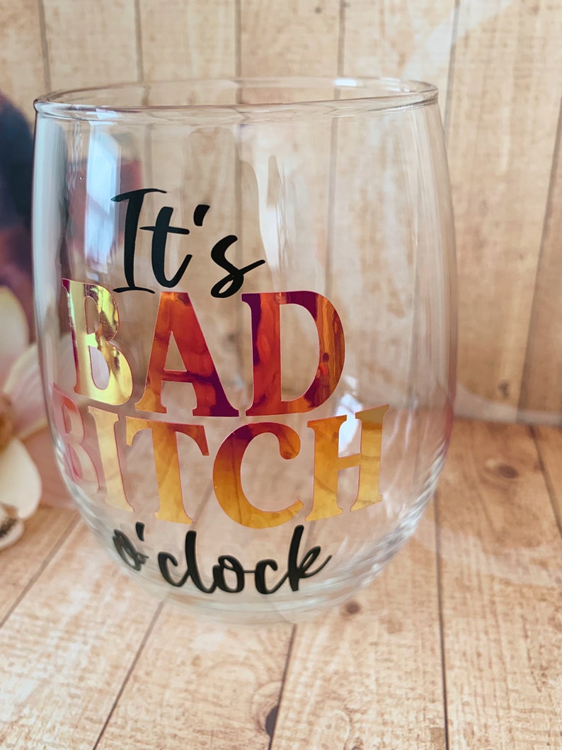 May include: Clear glass wine glass with the text "It's Bad Bitch o'clock" in black and gold foil lettering.
