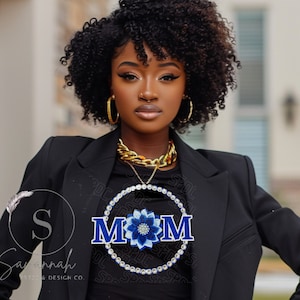 Puede incluir: Una camiseta negra con un diseño circular de diamantes de imitación que presenta la palabra "MOM" en letras azules con una flor azul y blanca en el centro.