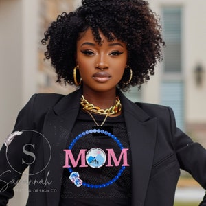 May include: A black t-shirt with a pink "MOM" graphic surrounded by a blue beaded circle. The graphic includes a family silhouette and the text "Save the Seal of Kindness, Inc. 1995".