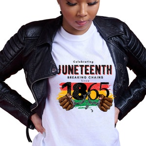 May include: White t-shirt with a black graphic design that says "Celebrating Juneteenth Breaking Chains Since 1865". The graphic features a red, yellow, and green striped background with two black hands in handcuffs.